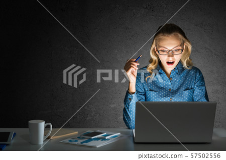 Attractive blonde working on laptop in dark office. Mixed media Attractive blonde working on laptop in dark office. Mixed media 57502556