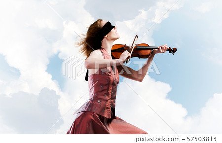 Woman violinist in red dress playing melody against cloudy sky Woman violinist in red dress playing melody against cloudy sky 57503813