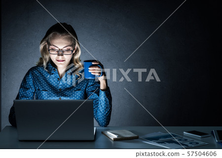 Attractive blonde working on laptop in dark office. Mixed media Attractive blonde working on laptop in dark office. Mixed media 57504606