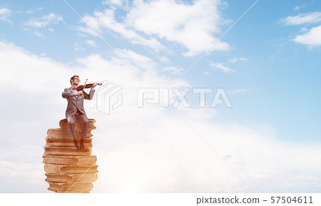 Handsome violinist in blue day sky on pile of books play his melody 57504611