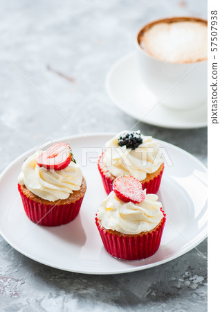 Three vanilla cupcakes with cappuccino on a gray Three vanilla cupcakes with cappuccino on a gray 57507938