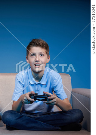 Gaming concept. Boy sitting on sofa playing video game with joystick 57510341