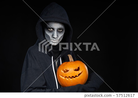 Boy with Halloween makeup holding Jack O'Lantern pumpkin on black background 57512617