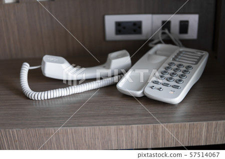 Remove headset of white vintage telephone with grey buttons on a brown table in hotel. 57514067
