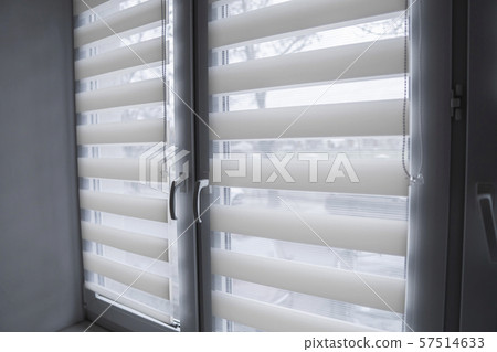 White fabric roller blinds on the white plastic window in the living room. Roll curtains indoor. 57514633