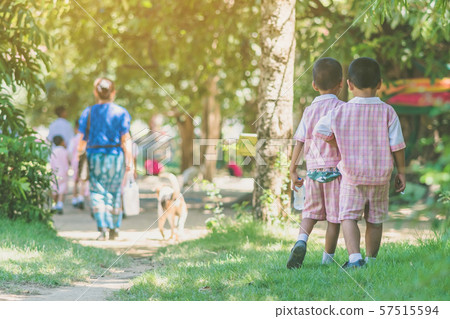 Kindergarten boy walk after female teacher and his friends back to class after having lunch. Kindergarten boy walk after female teacher and his friends back to class after having lunch. 57515594