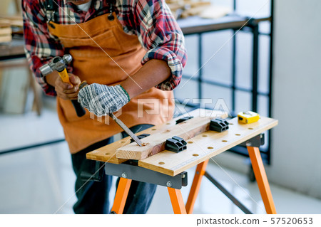 Old craftsman use hammer and chisel to work with wood and produce some product in his workplace 57520653