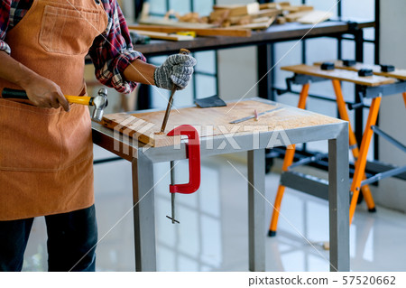 Old craftsman use hammer and chisel to work with wood and produce some product in his workplace 57520662