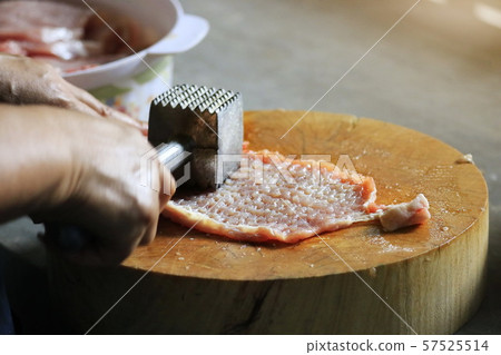 The man's hand picks up an iron hammer and smashed the pork on a wooden chopping board to make steak. The man's hand picks up an iron hammer and smashed the pork on a wooden chopping board to make steak. 57525514