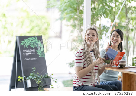 A Japanese woman smiling and talking with a foreign woman enjoying a coffee break at an open terrace cafe 57530288