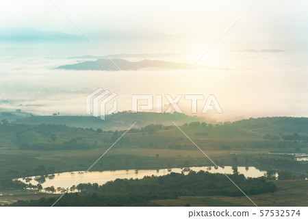 Mountain range with visible silhouettes through the morning colorful fog over pond water. 57532574