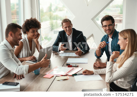 Teamwork. Multicultural team discussing something and smiling while sitting at the office table 57534271