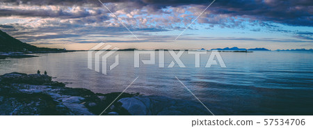 Panoramic photo of people sitting on a rocky seashore at sunset in Norway Panoramic photo of people sitting on a rocky seashore at sunset in Norway 57534706