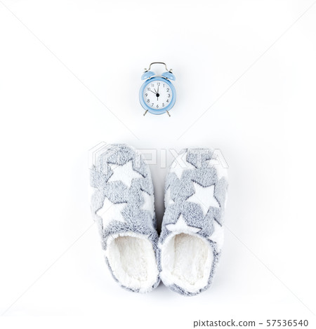 Soft fluffy slippers and blue alarm clock 57536540