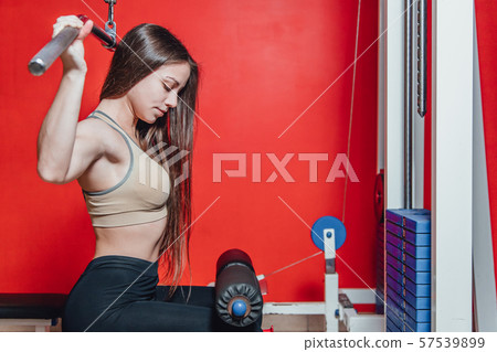Beautiful young girl engaged in fitness in the gym. Brunette performs exercises on the simulator. 57539899