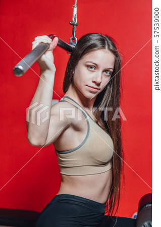 Beautiful young girl engaged in fitness in the gym. Brunette performs exercises on the simulator. Beautiful young girl engaged in fitness in the gym. Brunette performs exercises on the simulator. 57539900