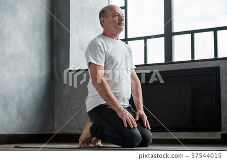 Senior hispanic man practicing yoga at home in vajrasana pose 57544015