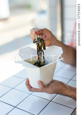 Close-up of man eating chinese noodles in a cafe. The concept of healthy Asian cuisine. Close-up of man eating chinese noodles in a cafe. The concept of healthy Asian cuisine. 57554003