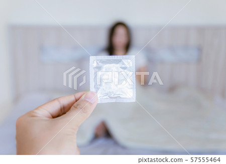 The man with the hand a condoms of the woman lying on the bed is blurred The man with the hand a condoms of the woman lying on the bed is blurred 57555464