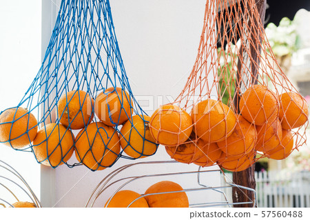 Fresh oranges hang in a mesh bag at the market. Fruit for fresh juice. Fresh oranges hang in a mesh bag at the market. Fruit for fresh juice. 57560488