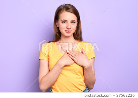 Adorable woman keeps both palms on heart, looks in camera with friendly smile Adorable woman keeps both palms on heart, looks in camera with friendly smile 57562226