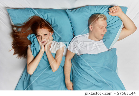 Unhappy woman closing her ears with palms and her snoring husband lying bedroom. Unhappy woman closing her ears with palms and her snoring husband lying bedroom. 57563144