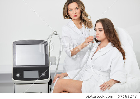 doctor doing rf-lifting procedure for young woman sitting in a beauty salon 57563278