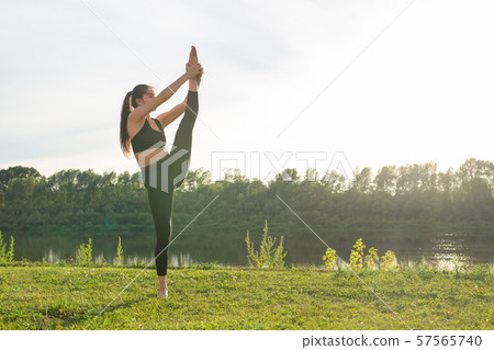 Harmony and healthy lifestyle concept - Young slim woman in sportswear practicing yoga outdoors. 57565740