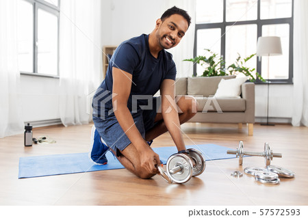 smiling indian man assembling dumbbells at home smiling indian man assembling dumbbells at home 57572593