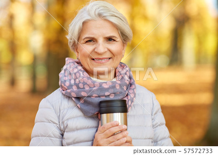 old woman with hot drink in tumbler at autumn park 57572733