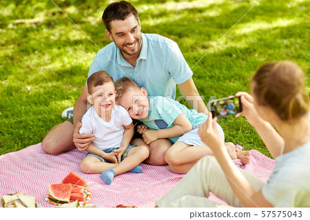mother taking picture of family on picnic at park 57575043