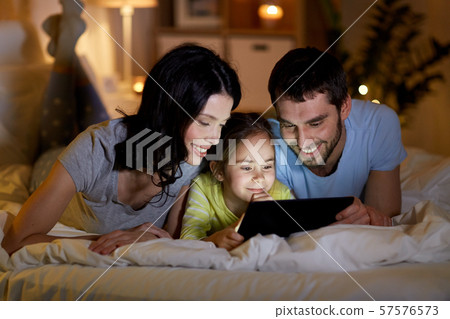 family with tablet pc in bed at night at home family with tablet pc in bed at night at home 57576573