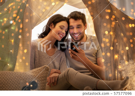 happy couple with smartphone in kids tent at home happy couple with smartphone in kids tent at home 57577096