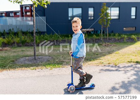 happy little boy riding scooter in city 57577199