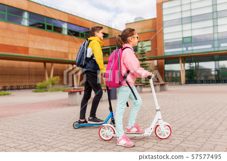 school children with backpacks riding scooters 57577495