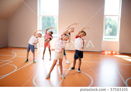 Boys and girls stretching with teacher at the PE lesson Boys and girls stretching with teacher at the PE lesson 57583105