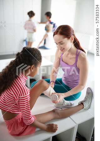 Teacher providing first aid to girl with knee ache 57583334