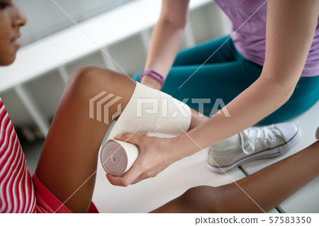 Teacher providing first aid while putting bandage on knee Teacher providing first aid while putting bandage on knee 57583350