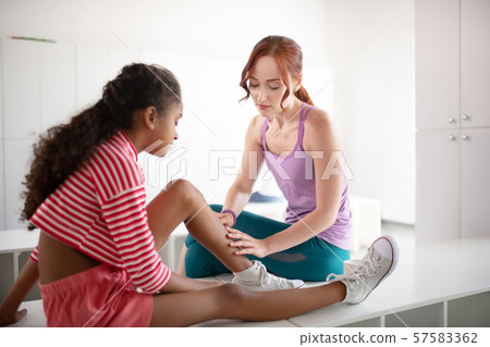 Red-haired PE teacher helping girl with knee trauma 57583362