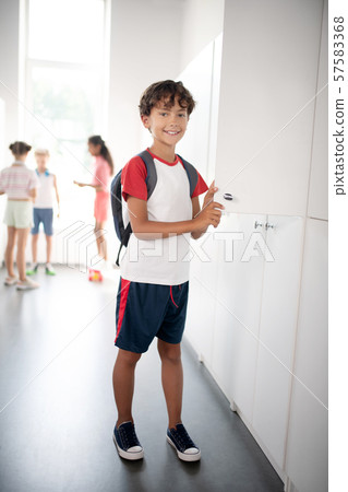 Dark-haired boy wearing sport clothing standing near locker 57583368