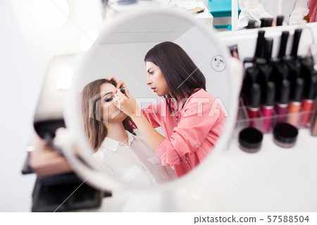 Make-up artist applying bright base color eyeshadow on model's eye and holding a shell with 57588504