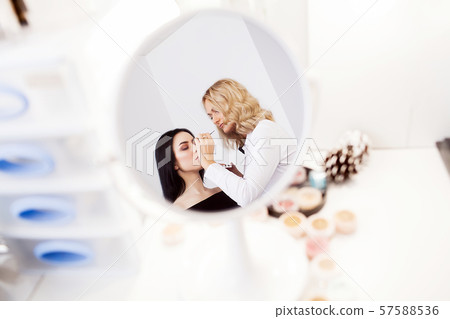 Make-up artist applying bright base color eyeshadow on model's eye and holding a shell with Make-up artist applying bright base color eyeshadow on model's eye and holding a shell with 57588536