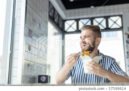 Positive young stylish guy eating chinese noodles in a cafe during a break at work. The concept of Positive young stylish guy eating chinese noodles in a cafe during a break at work. The concept of 57589814