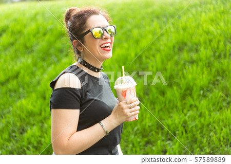 Portrait of a positive young pretty girl in punk clothes and glasses with a milkshake in her hands Portrait of a positive young pretty girl in punk clothes and glasses with a milkshake in her hands 57589889