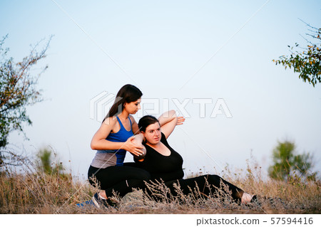 Trainer assisting overweight woman doing sit-ups Trainer assisting overweight woman doing sit-ups 57594416