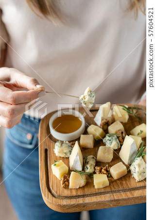 Girl holding piece of Gorgonzola cheese on a skewer and wooden plate with cheese. Delicious cheese Girl holding piece of Gorgonzola cheese on a skewer and wooden plate with cheese. Delicious cheese 57604521