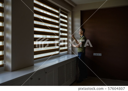 The man is opening the blinds. The man is opening the blinds. 57604807