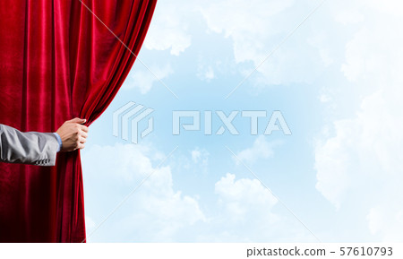 Cloudy landscape behind red curtain and hand holding it 57610793