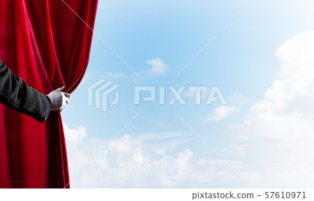 Cloudy landscape behind red curtain and hand holding it 57610971