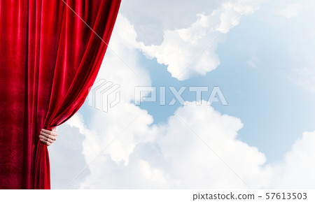 Cloudy landscape behind red curtain and hand holding it 57613503